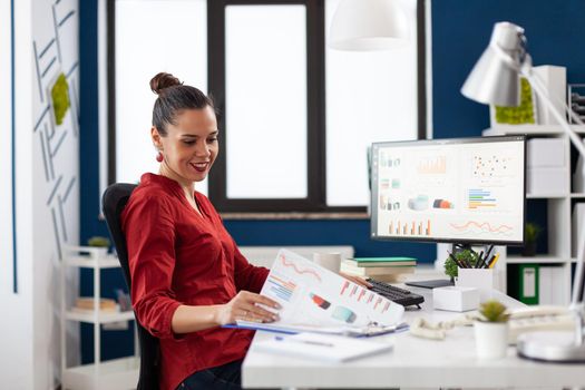 Business woman in start up company working on computer and analyzing charts on clipboard, sitting at desk. Successful concentrated manager working on deadline project typing.