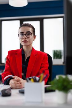 Successful businesswoman in corporate financial company office, looking at camera sitting at desk. Entrepreneur start up leadership wearing glasses. Financial adviser worker with with charts on clipboard.