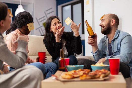 Cheerful group of colleagues enjoying a game of charades after work at office. Multi ethnic people play imitation concept for fun activity entertainment while eating pizza and drinking beer