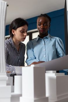 Multi ethnic work team looking at building model maquette design. Professional women architects working on designer project at desk for urban development engineering industry