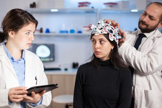 Professional neurological researcher explaning treatment result pointing on monitor while medical scientist adjusting eeg headset, preparing for brain scan analysing electrical activity, nervous system.