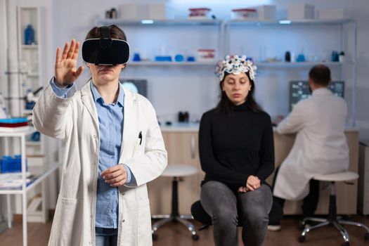 Professional researcher wearing virtual reality glasses using medical inovation in lab analysing brain scan of patient. Team of neurological doctors working with equipment high tech simulator device.