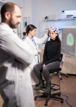 Neuroscience scientist adjusting headset with sensors on womna patient in modern lab during brain scanning. Nervous system analysis, clinic equipment. Doctor brain scan.