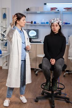 Scientist doing brain analysis using headset with sensors on patient explayning diagnosis. Monitor shows modern brain study. Wearing neuroscience headset analysis.