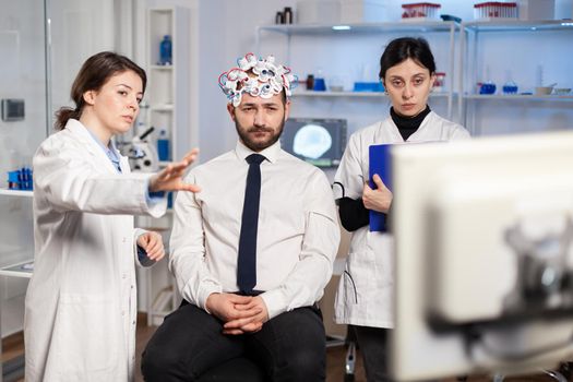 Neurological researchers explaning treatment result pointing on monitor while medical scientist adjutaking notes, scanning headset preparing for brain scan analysing electrical activity.