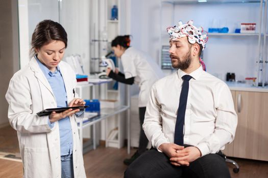 Neuroscience doctor using tablet pc treatment against brain disease explaning to patient diagnosis of illness. Woman sitting in neurological scientific lab treating nervous system dysfunctions.