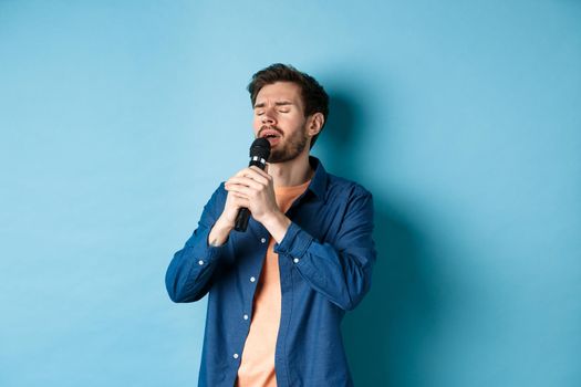 Romantic guy singing in microphone, performing on stage, standing on blue background.