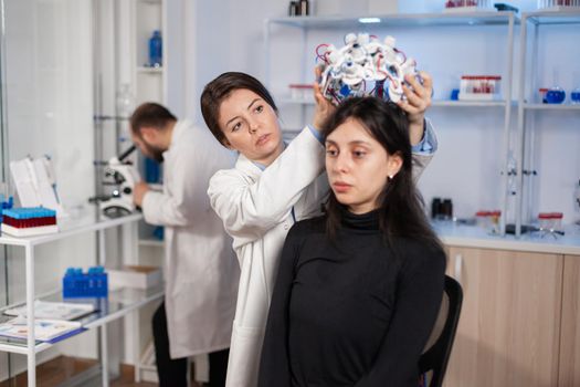 Medical lab technician putting eeg headset monitoring brain functions, descovering diagnosis of disease. Team of scientists researchers working late night in neurology clinic for woman health.