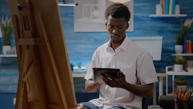 African american adult with artistic skills using digital tablet for drawing design in artwork space at home. Black young artist working on canvas and easel for masterpiece with technology