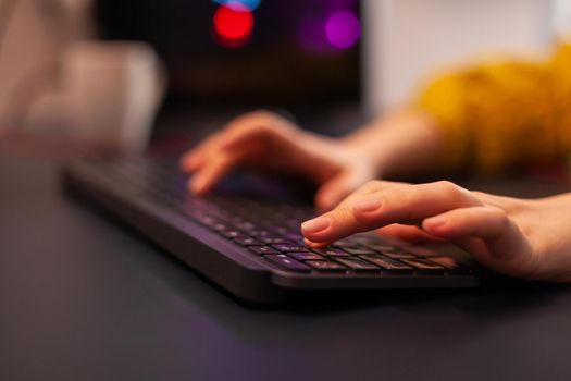 Close-up on hands of woman gamer playing video game using keyboard. Virtual championship in cyberspace, esports player performing on pc during gaming tournament using technology network wireless.