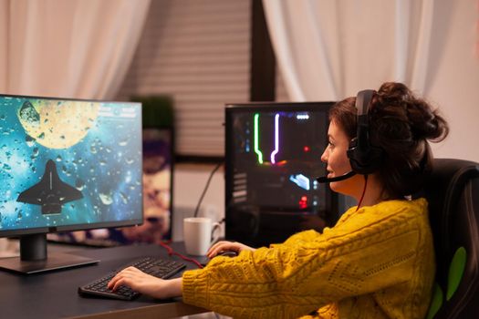 Expert woman gamer playing space shooter video game on powerful PC. Virtual shooter game championship in cyberspace, esports player performing on computer in stylish room during gaming tournament.