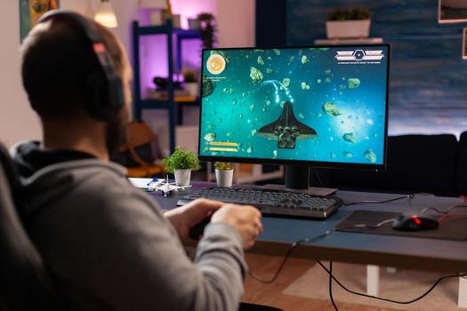 Gamer player with headphones performing videogame with modern graphics for space shooter championship. Online streaming cyber performing during gaming tournament using technology network wireless