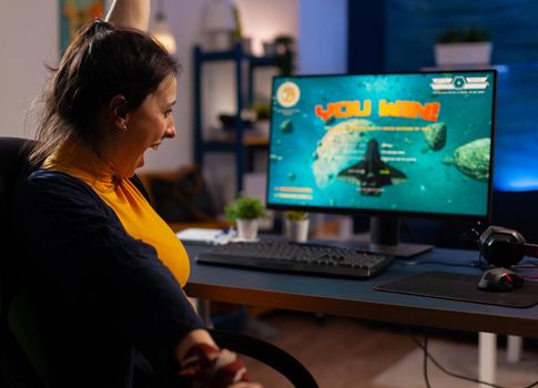 Winner player sitting on gaming chair at desk and playing space shooter video games with joystick. Woman streaming online videogames for esport tournament in room with neon lights