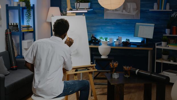 Black artist using pencil on canvas to draw vase in art space at home. African american creative man working on masterpiece design for artwork concept. Person with skill and imagination