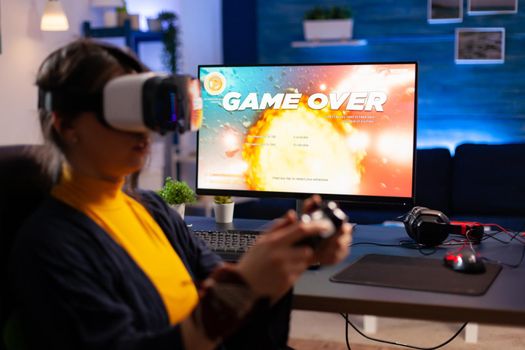 Game over for cyber gamer playing space shooter game using professional vr headphones. Defeated player using joystick for online championship sitting on gaming chair late at night in living room