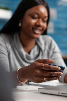 Afro american woman holding economy credit card doing online shopping sitting on bean bag in living room. Black student using internet banking service on laptop computer making store ordering