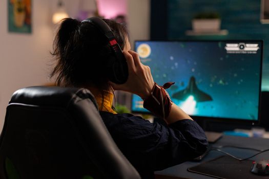 Woman videogamer using powerful computer playing online videogames in gaming home studio. Virtual streaming cyber uwearing headphones performing gaming tournament using professional equipment.