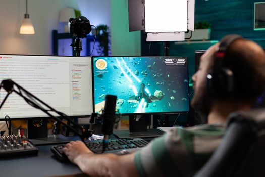 Streamer playing videogames and talking with teammates on streaming open chat. Cyber performing on powerful computer in gaming room home using professional equipment