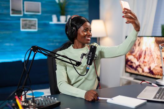 African influencer recording podcast and taking selfie in home studio. On-air online production internet podcast show host streaming live content, recording digital social media.
