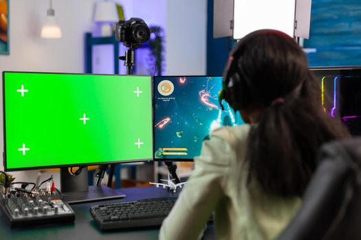 Back view of black gamer streams online game tournament on computer with green screen at night. Gamer using pc with greenscreen isolated desktop streaming space shooter video games.