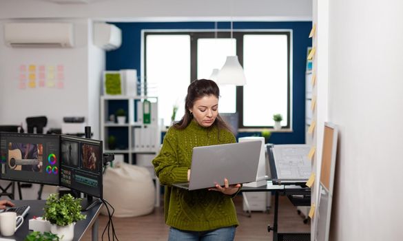 Employee holding laptop standing in creative agency office prosessing customer video project in post production software. Videographer working in digital multimedia company editing movie footage