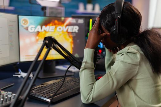 Sad african e sports streaming after losing online competition covering face wearing headphones. Professional gamer streaming online video games with new graphics on powerful computer.