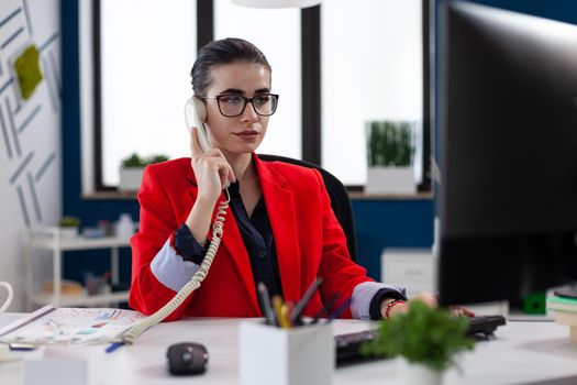 Businesswoman having a phone coversation with financial adviser sitting at desk looking at charts on computer screen. Company executive answering taking a cellphone call.