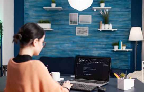 Back view of student developer writing javascript using analytic program while sitting at desk table in living room. Freelancer software developer programer programming digital code