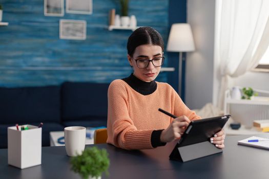 Creative student drawing on digital tablet using graphic pen sketching ilustration draw. Concentrated young illustrator sitting at desk table in living room retouching sketch with retoucher tools