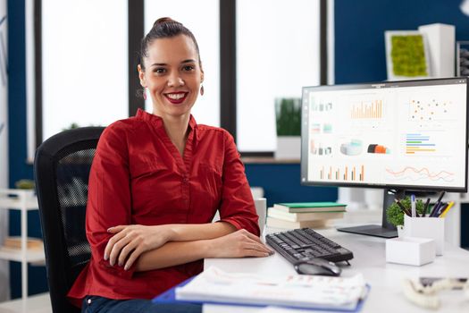 Portrait of business woman in corporate office sitting at desk smiling at camera. Company executive leadership working on financial statistics. worker doing charts on computer.