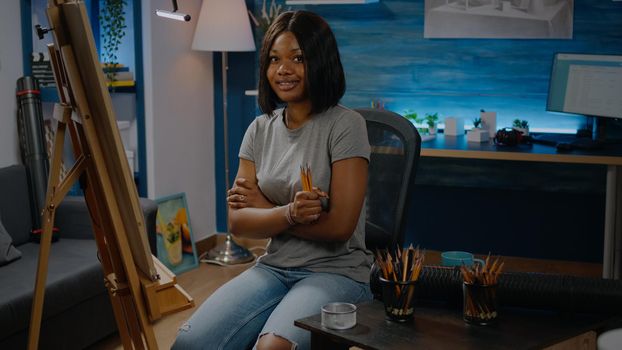 African american young woman holding colorful pencils prepared to draw on white canvas sitting in artwork studio. Black artist with creative inspiration ready for masterpiece design