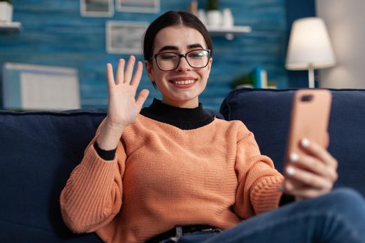 Happy student having online videocall meeting on smartphone with her friends consulting about social media communication. Teenager lying on couch in living room watching at screen phone