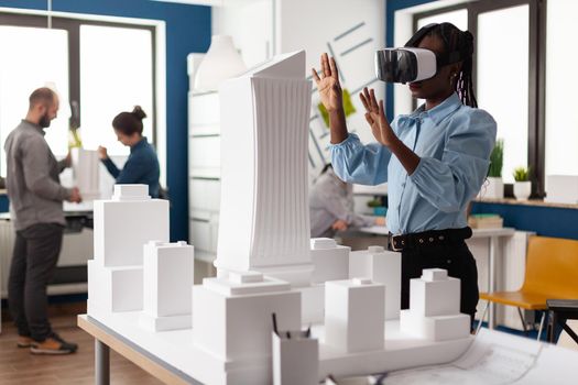 African american woman using vr glasses at work for 3d visual simulation. Standing businesswoman working on building model maquette with modern digital plan design technology
