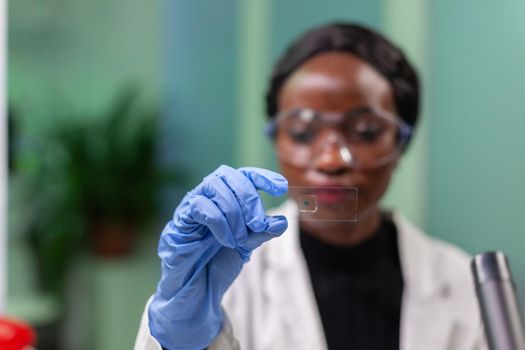 African botanist woman looking at genetic test sample for biological experiment. Pharmaceutical scientist analyzing organic agriculture in microbiology scientific lab working at biochemistry expertise.