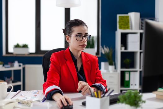 Focused businesswoman in corporate office workplace, working on computer, making financial analysis. Concentrated entrepreneur using mouse with wireles technology sitting at desk.