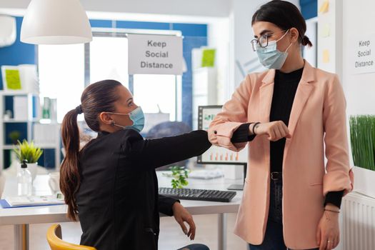 Office workers saying hello touching elbow wearing face mask as safety precaution during global pandemic with coronavirus, to avoid infection with covid-19 keeping social distancing.