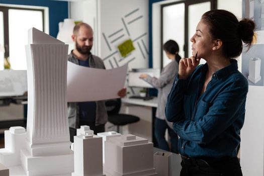 Professional architects working on blueprints plan to design building model maquette construction layout. Team of caucasian workers discussing industry project for engineering