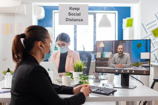 Coworkers discussing project during remote call from new workplace in time of global pandemic with coronavirus, wearing face mask as prevention to covid flu.
