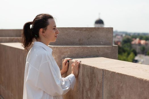 Caucasian female enjoying looking at metropolitan city from panoramic terrace of bulding tower enjoying summer vacation. View of city skyline from observation point. Panoramic view of buildings