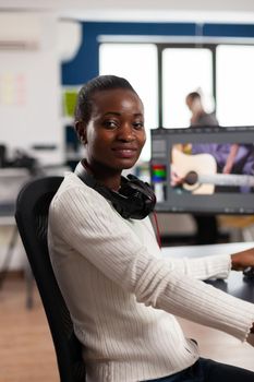 African video editor looking at camera smiling editing video project in post production software working in creative studio office. Videographer editing audio film montage on professional computer