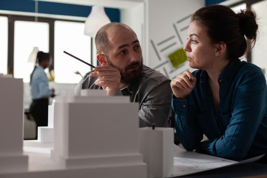 Engineering group of architects sitting at office discussing work plan for maquette design building model. Professional architecture workers talking about digital construction layout