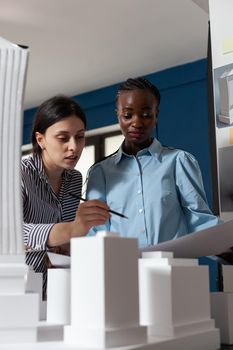 Multi ethnic work team looking at building model maquette design. Professional women architects working on designer project at desk for urban development engineering industry