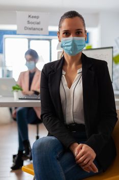 Close up portrait of business employee in working space wearing face mask as safety precation during global pandemic with coronavirus looking at camera.