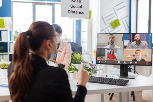 Entrepreneur woman on remote video conference discussion in new normal workplace during global pandemic with covid19 flu, wearing face mask keeping social distancing. Internet web videocall chat online talk