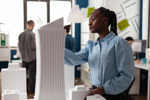 African american architect constructor at office working on building model plan design maquette. Afro woman looking at modern layout of construction for development project