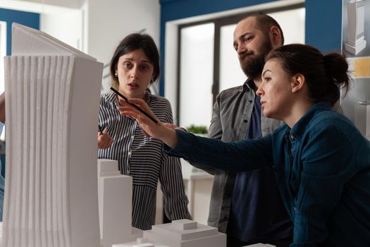 Professional team of architects analyzing maquette building model. Group of engineer partners working on project design for construction plan explaining modern blueprint vision.