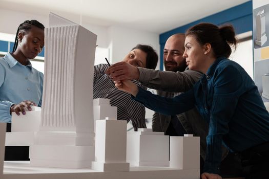 Group of multi ethnic colleagues work in architecture at project with blueprint plans building model maquette. Professional partners discussing vision of construction design on paper