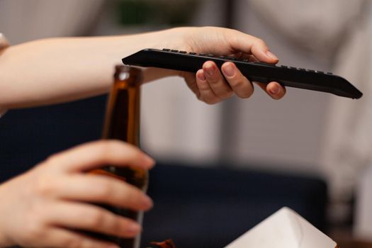 Close-up of woman hands changing channels using remote watching entertainment comedy movie film on television in evening. Caucasian female relaxing having takeaway food home delivered