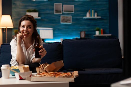 Happy woman sitting on sofa watching comedy movie film on television in evening eating tasty delicious snack. Caucasian female enjoying takeaway food home delivered. Junck-food lunch order