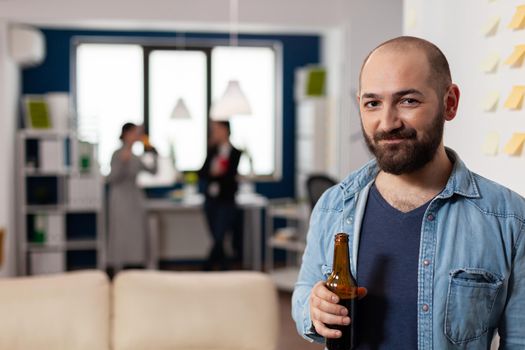 Caucasian man smiling and holding bottle of beer after work at office party. Colleagues meeting for fun activities enjoyment while playing games eating drinking alcohol. Celebration drinks